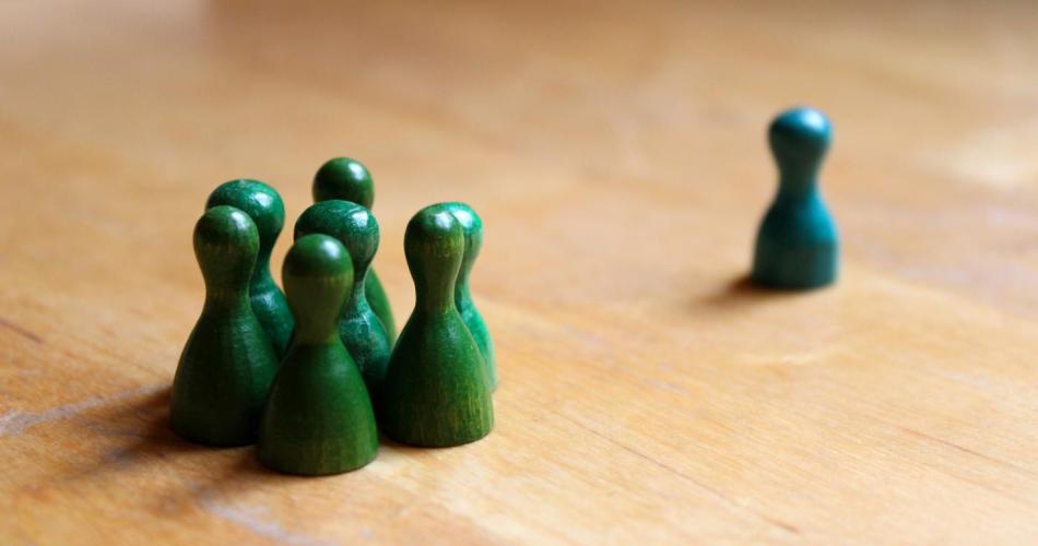 Symbolbild Mobbing: Eine Gruppe grüner Spielkegel steht einem einzelnen Spielkegel gegenüber